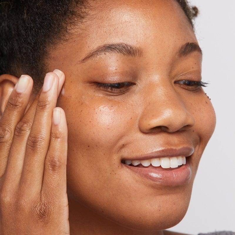 Eine Frau mit reiner Haut lächelt und berührt sanft ihr Gesicht, wodurch die strahlende Wirkung des Biolumin-C Augenserums hervorgehoben wird.