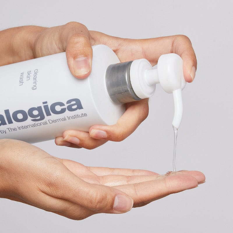 Eine Hand pumpt vor einem schlichten Hintergrund Clearing Skin Wash, einen reinigenden Schaumgel-Cleanser mit Teebaumöl, aus einer weißen Dermalogica-Flasche auf die Handfläche einer anderen Hand.