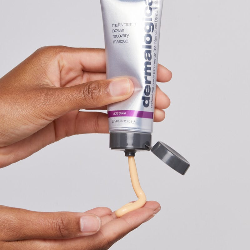 Eine Person gibt eine beige Creme aus einer Tube mit der Aufschrift „MultiVitamin Power Recovery Masque“ auf ihre Handfläche – Teil des Stressed Skin Recovery System Set für antioxidantienreiche Anti-Aging-Hautpflege.