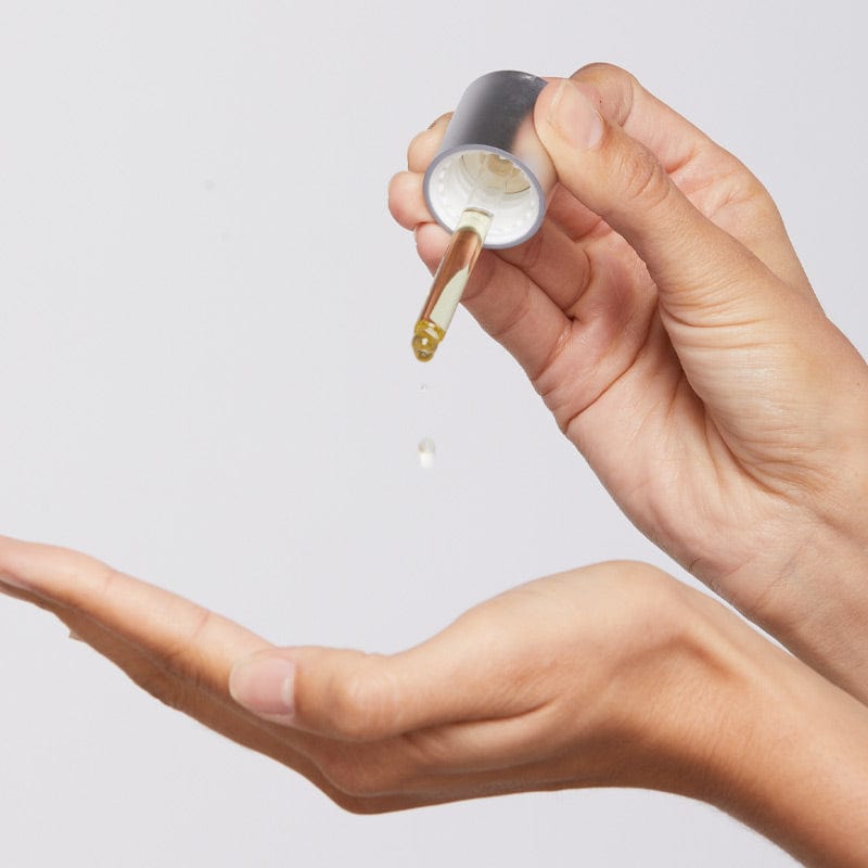 Eine Hand hält eine Pipette über einer offenen Handfläche und gibt einen Tropfen Retinol Clearing Oil auf die Haut vor einem schlichten hellen Hintergrund ab – perfekt für Ihre Nachtpflege.