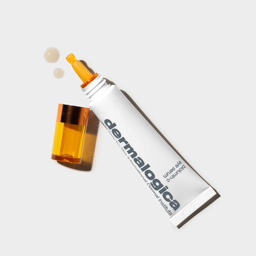 Eine Tube Biolumin-C Augenserum mit abgenommener orangefarbener Kappe und zwei Tropfen daneben, abgebildet auf weißem Hintergrund. Dieses Serum ist dafür bekannt, den Hautton auszugleichen und sichtbare Zeichen der Hautalterung zu reduzieren.