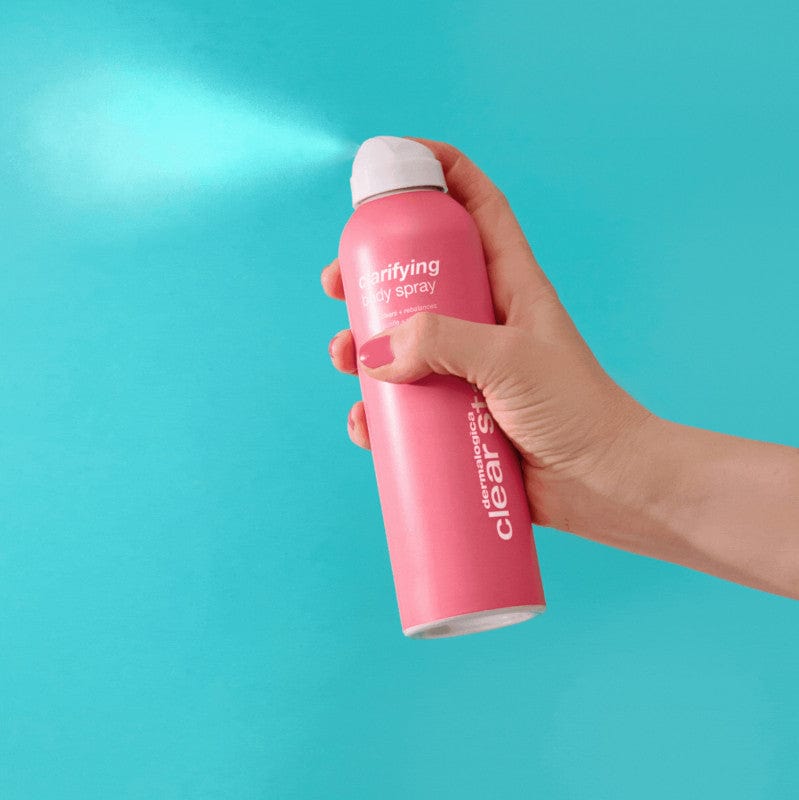 Eine Hand sprüht vor einem blauen Hintergrund aus einer rosa Dose Clarifying Body Spray + Daily Microfoliant und bekämpft gezielt Körperunreinheiten für frische, reine Haut.