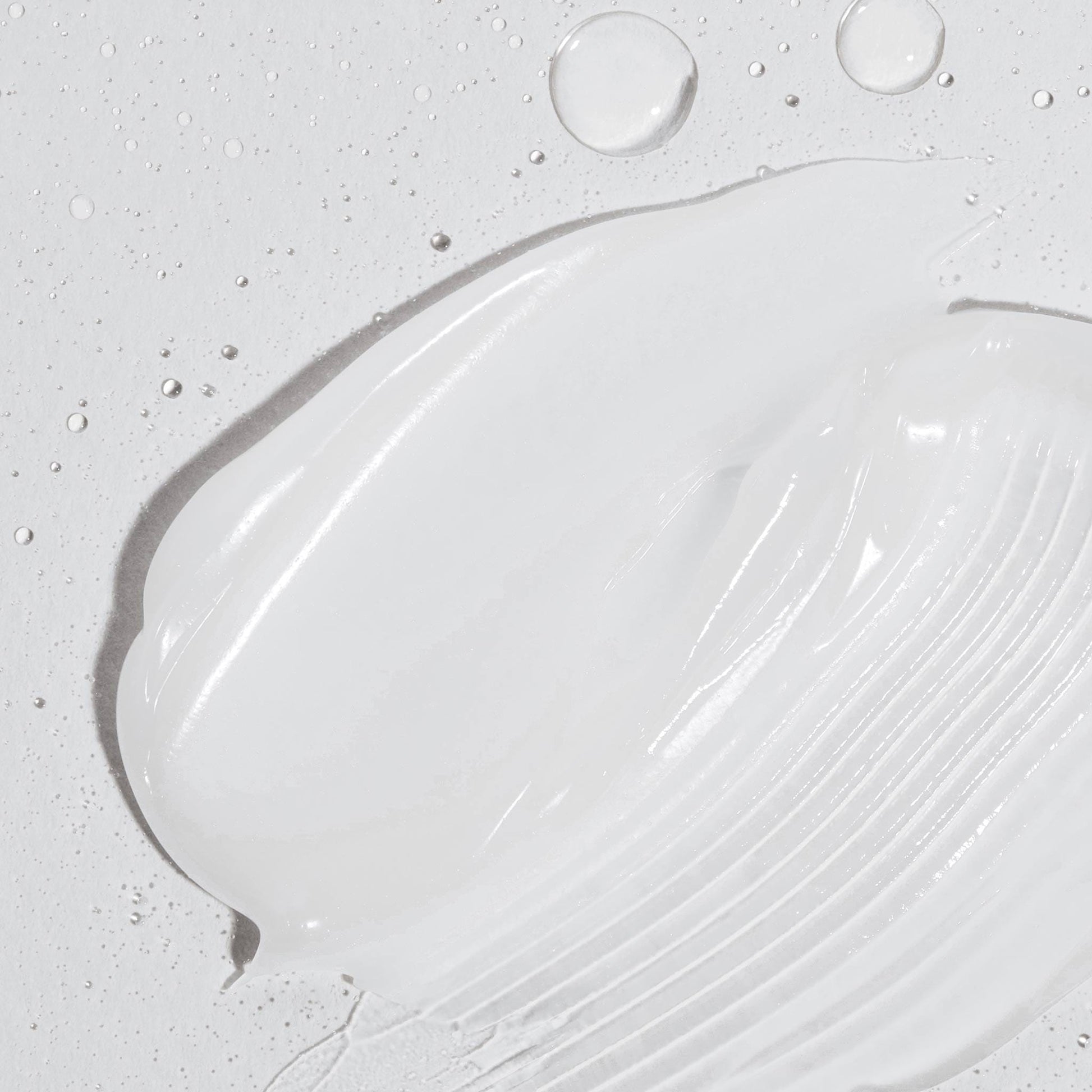 Eine Nahaufnahme der weißen Creme aus dem Sensitive Rescue Kit, die mit Wassertropfen auf eine strukturierte Oberfläche aufgetragen wurde – perfekt für empfindliche Haut und inspiriert von Dermalogica Produkten für ultimative Feuchtigkeit.