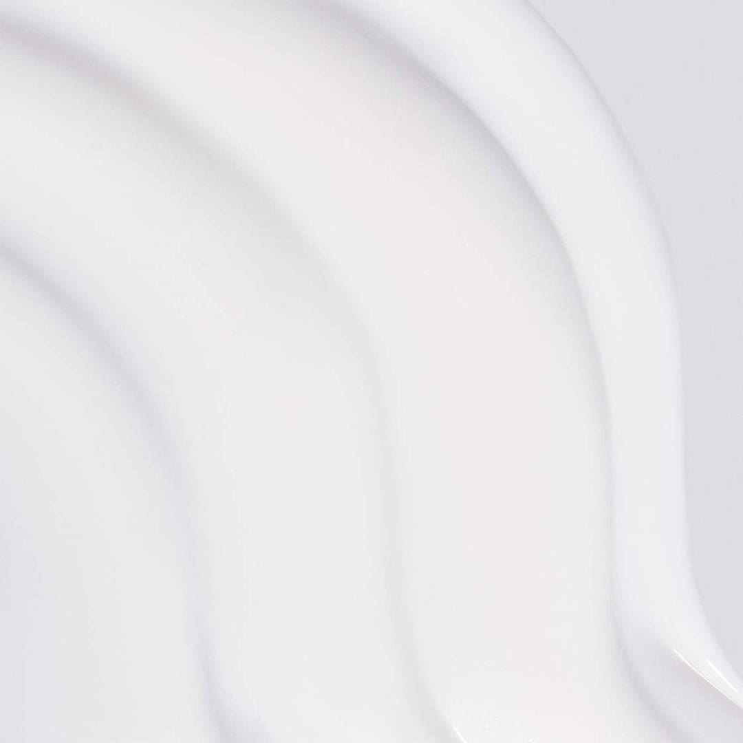 Nahaufnahme des glatten, weißen, cremigen Skin Resurfacing Cleansers mit geschwungenen Texturen auf hellem Hintergrund, angereichert mit antioxidativem Vitamin E und pflegendem Rosenöl.