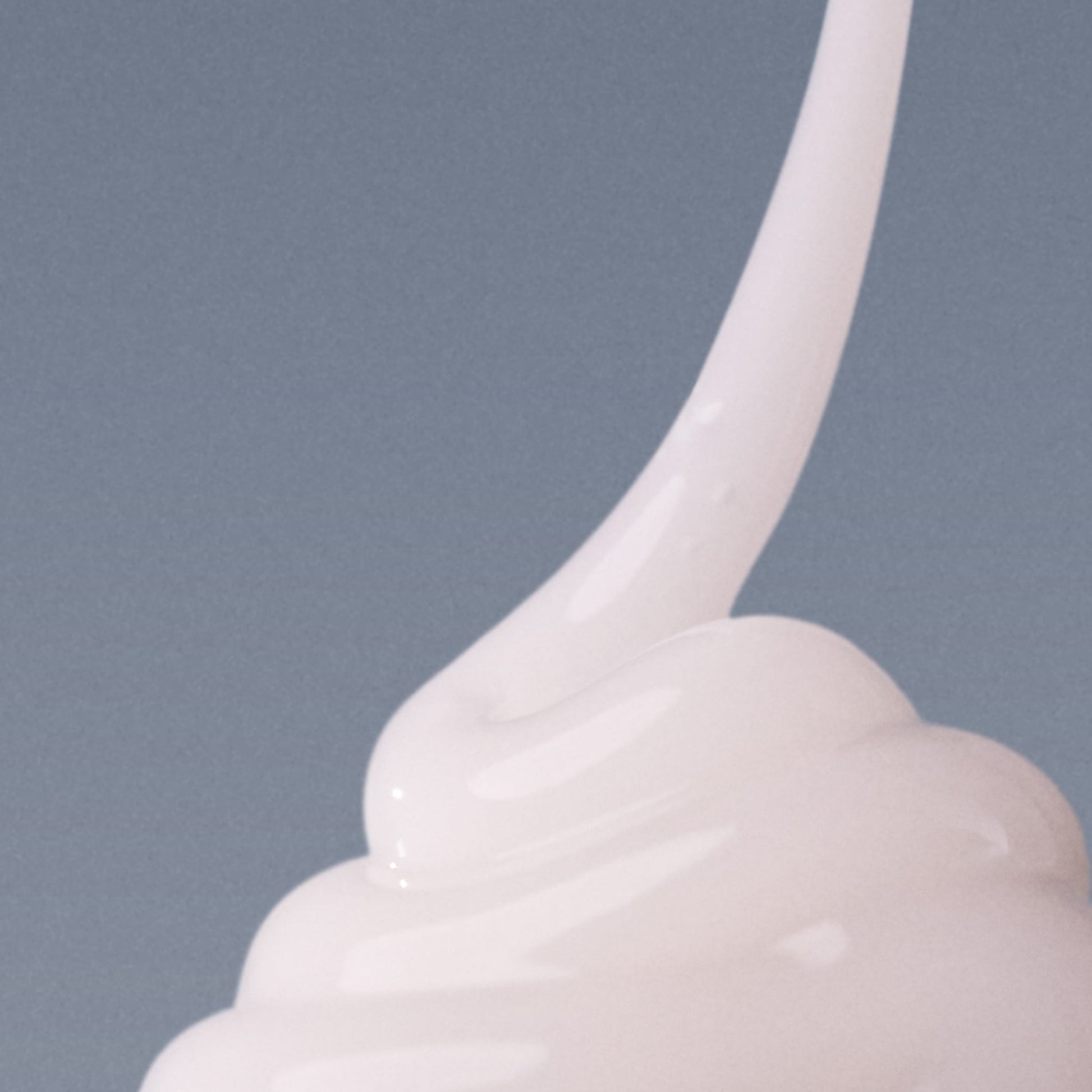 Ein Wirbel aus dicker, weißer Creme, der an das Pro-Collagen Banking Serum erinnert, hebt sich von einem schlichten grauen Hintergrund ab.