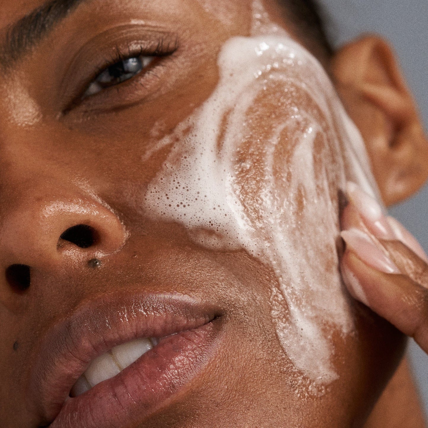 Eine Person trägt mit den Fingern sanft „PreCleanse“ und anschließend den schäumenden Gesichtsreiniger „Special Cleansing Gel“ auf ihre Wange auf und demonstriert damit eine durchdachte Hautpflegeroutine.