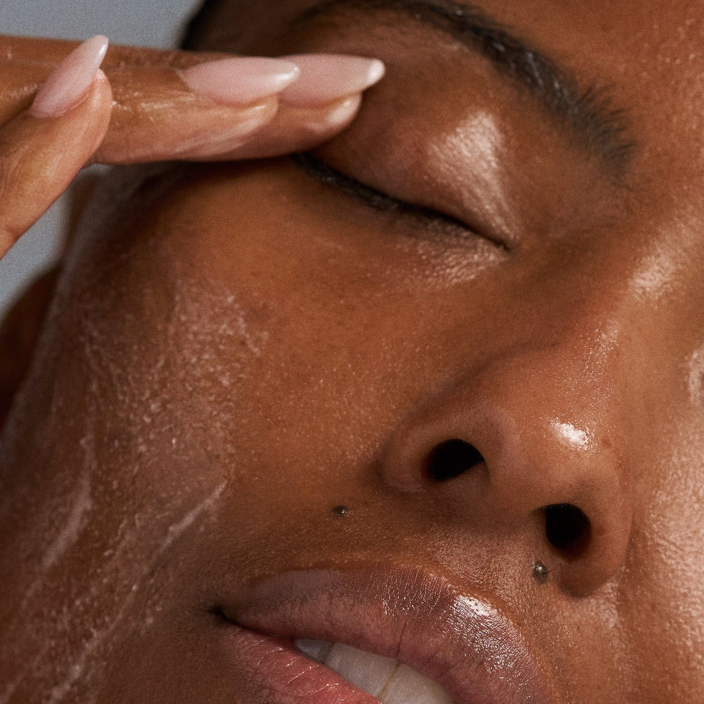 Mit geschlossenen Augen trägt eine Person mit der Fingerspitze zunächst PreCleanse und anschließend das Special Cleansing Gel auf ihr Gesicht auf, wobei glatte Haut und gepflegte Nägel zum Vorschein kommen.