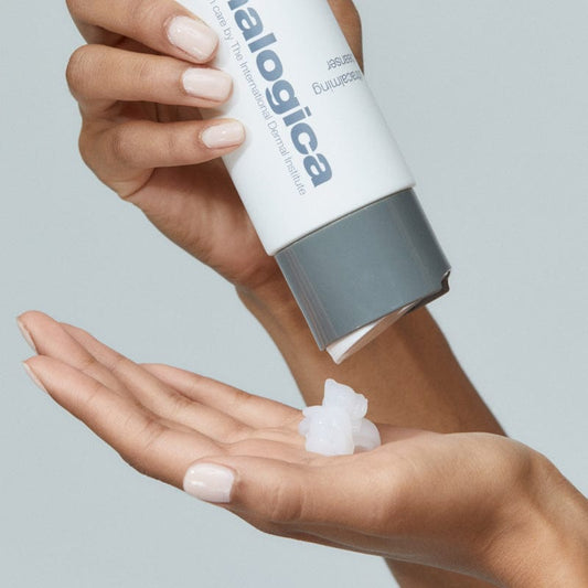 Eine Person gibt Stabilizing Repair Cream + UltraCalming Cleanser, ideal für empfindliche Haut, aus einer weißen Dermalogica-Tube in ihre Hand; eine Nahaufnahme zeigt sauber manikürte Nägel.