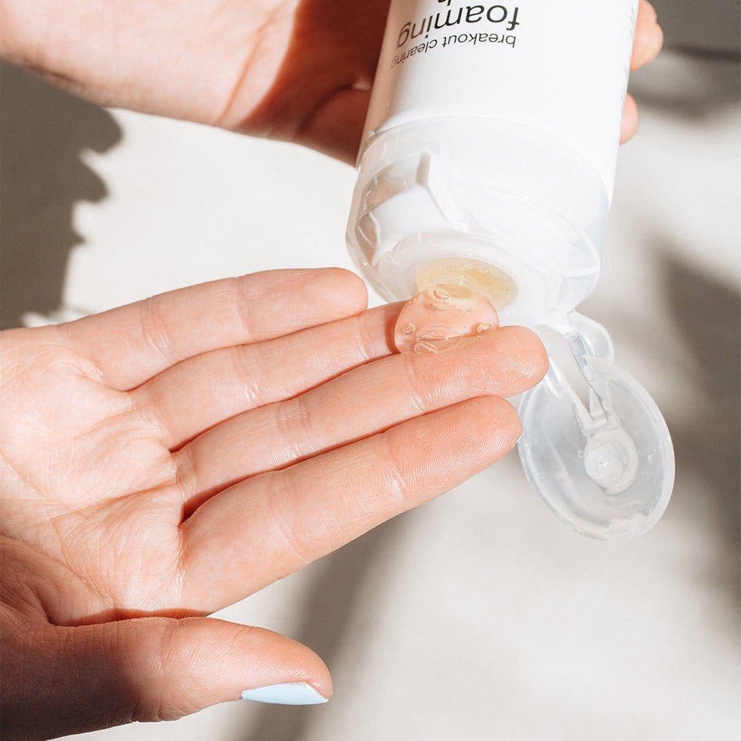 Eine Person gibt Breakout Clearing Booster + Breakout Clearing Foaming Wash aus einer weißen Tube auf ihre Fingerspitzen, bereit, Unreinheiten zu bekämpfen.