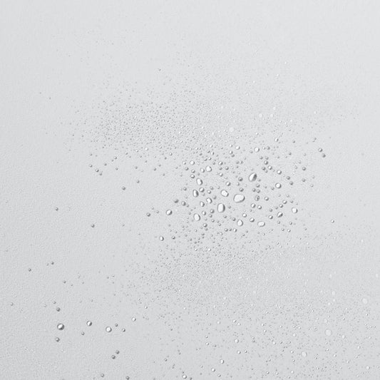 Gotas de líquido transparente de diferentes tamaños sobre una superficie lisa y de color claro.