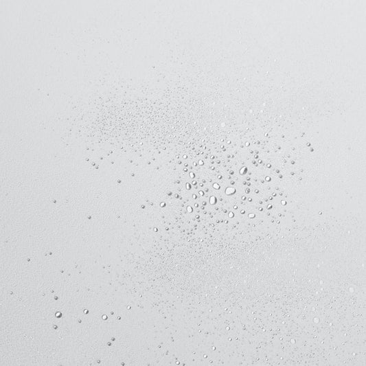 Tropfen klarer Flüssigkeit in verschiedenen Größen auf einer glatten, hellen Oberfläche.